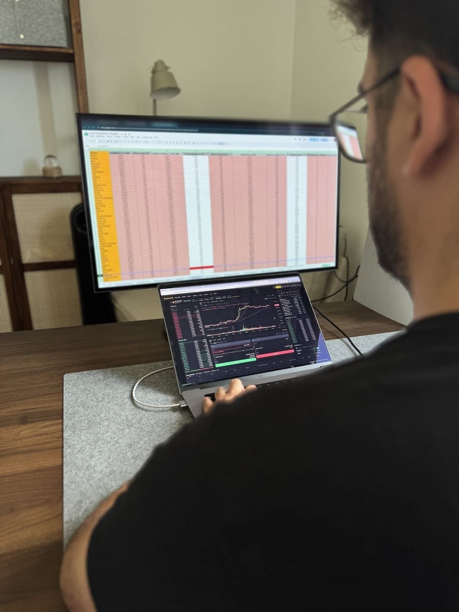 Peed am Schreibtisch: auf dem oberen Bildschirm die Bewertungsmatrix als Tabelle, auf dem Laptop darunter die Handelsansicht einer Krypto-Börse.